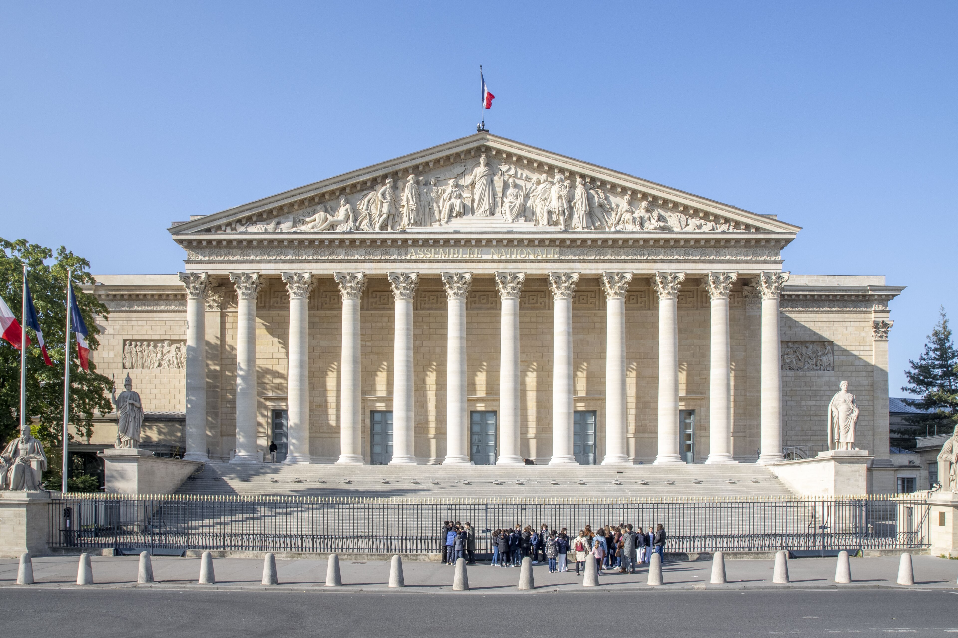 Façade du Palais Bourbon vue de la place de la Concorde : colonnade, fronton sculpté, grille et groupe de visiteurs.