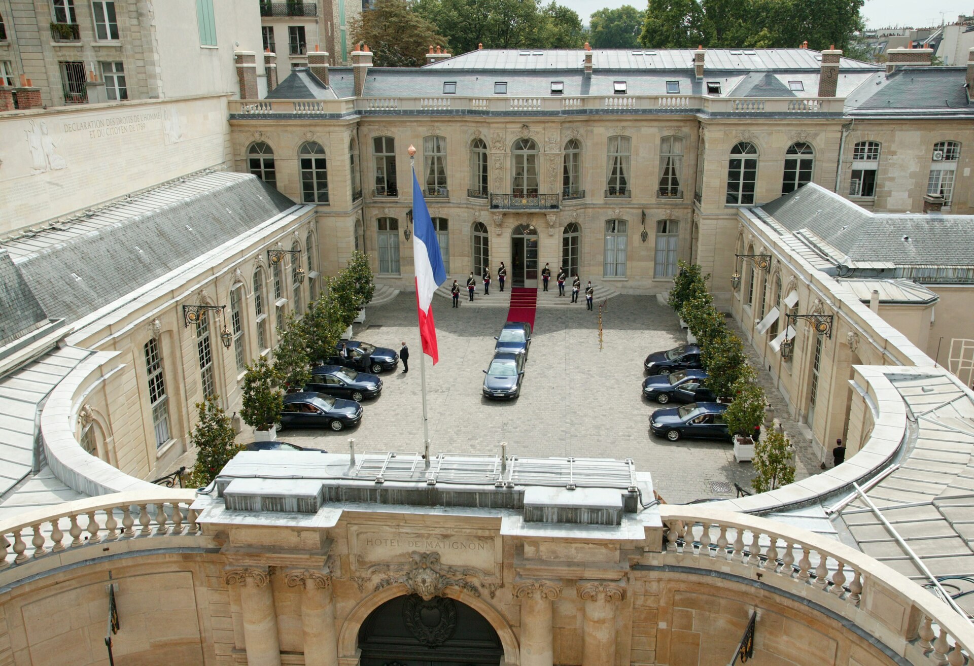 Cour de l’hôtel de Matignon vue du haut : drapeau, tapis rouge, cortège et inscription HOTEL DE MATIGNON.